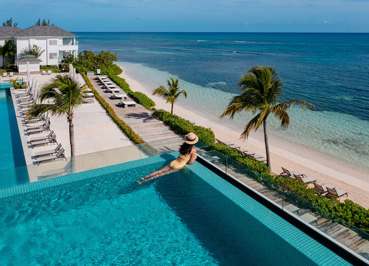 Woman on vacation at Excellence Oyster Bay relaxing in a pool looking out to the horizon and beach